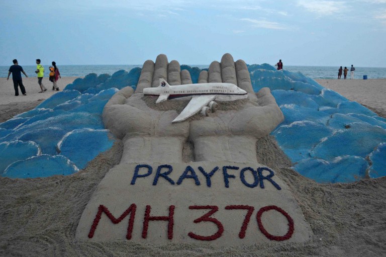 Beachgoers walk past a sand sculpture made by Indian sand artist Sudersan Pattnaik with a message of prayers for the missing Malaysian Airlines flight MH370 - which vanished from radar early on March 8 with ongoing search operations mounted by multiple nations taking place in the South China Sea, the Malacca Strait, and the Andaman Sea - at Puri beach, some 65 kilometers away from Bhubaneswar, on March 14, 2014. Malaysia denied March 12 that the hunt for a missing jet was in disarray, after the search veered far from the planned route and China said that conflicting information about its course was "pretty chaotic". AFP PHOTO/ ASIT KUMAR